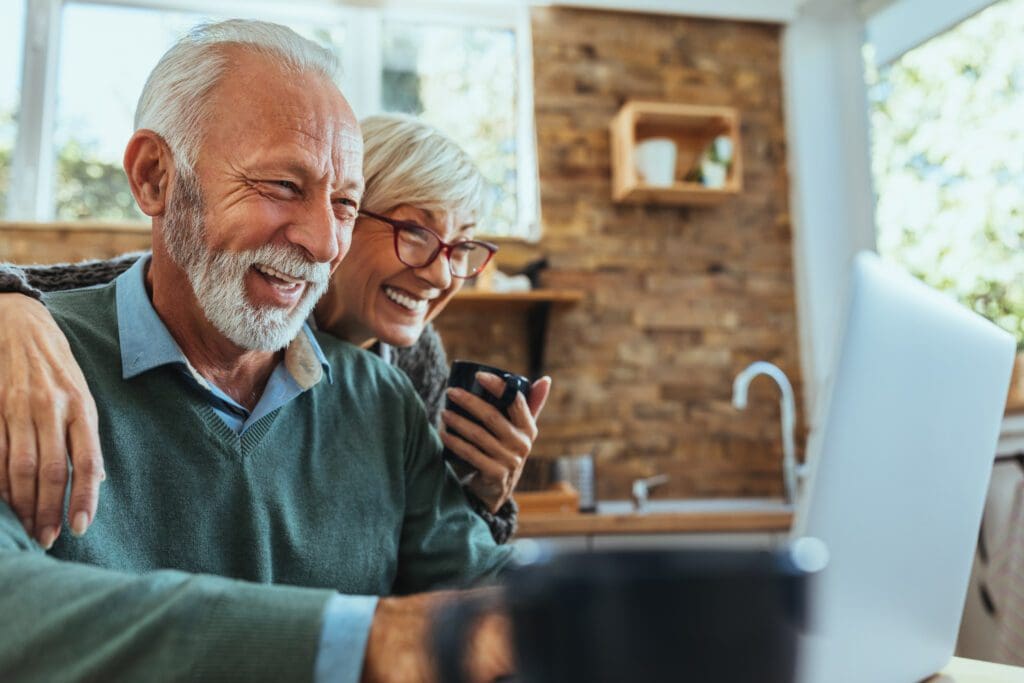 An older couple looks at their computer and smiles