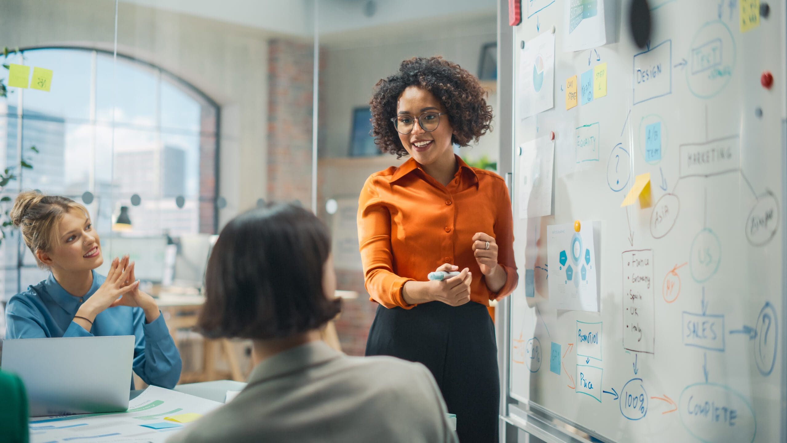 A young woman stands in front of a whiteboard and explains a series of investment strategies.